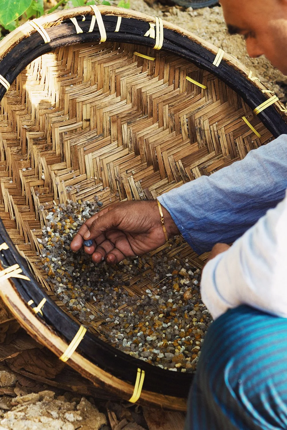 A gem miner sorting rough gemstones in a woven basket