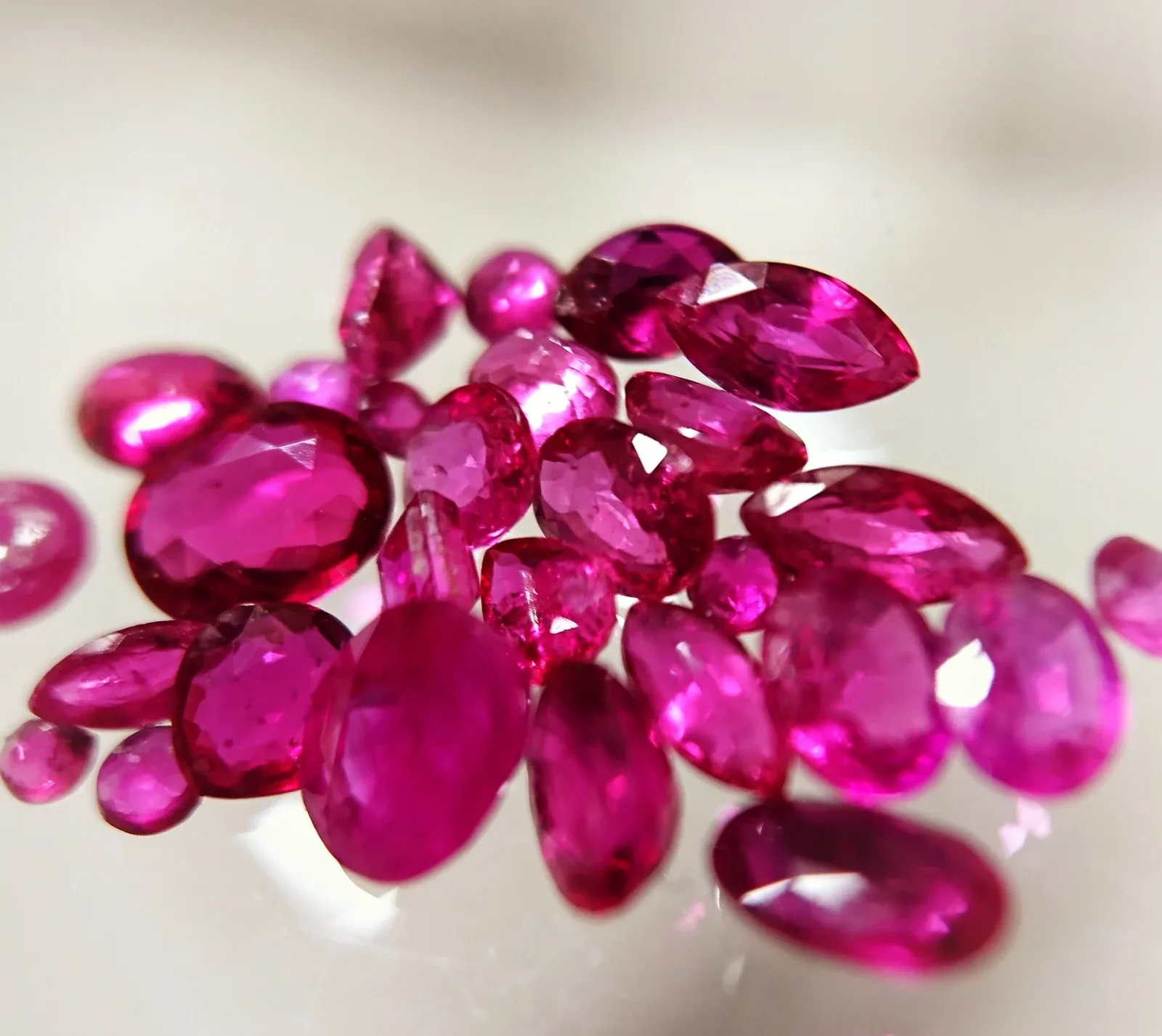 A group of faceted red and pink rubies photographed on a pale background