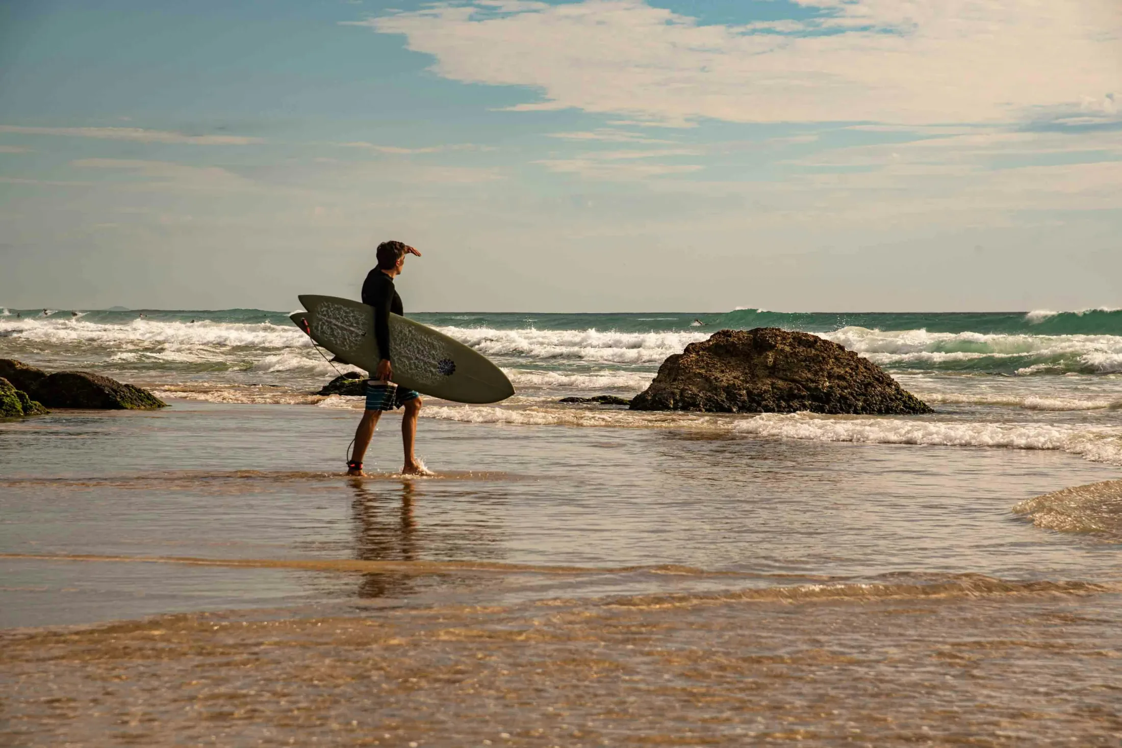 A surfer walking along a rocky tropical beach